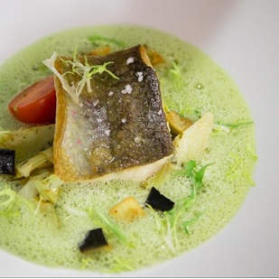 Filetto di pesce con pelle croccante su spuma verde, verdure e pomodoro.
