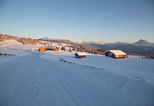 Snowy alpine huts at sunset, surrounded by mountains and freshly groomed cross-country track.
