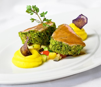 Zartes Fleisch im Kräutermantel mit Püree, Gemüsewürfeln und violetter Chips-Garnitur.
