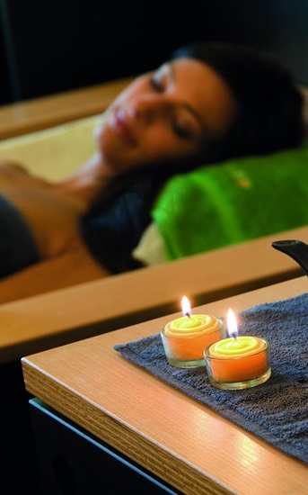 Woman relaxing in spa with lit candles and tea in foreground
