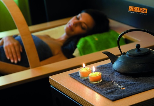 Woman relaxing in spa with lit candles and tea in foreground