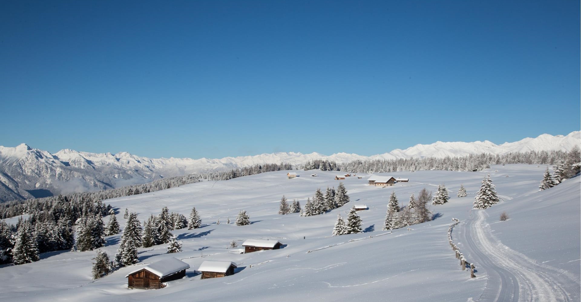 Winter scenery with snow-covered huts, trees, and cross-country ski trail in the mountains.