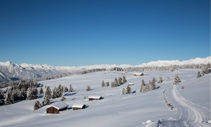 Winter scenery with snow-covered huts, trees, and cross-country ski trail in the mountains.