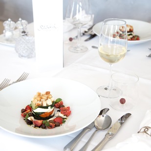 Appetizer with zucchini, cherry tomatoes, cheese and croutons on white table with wine.