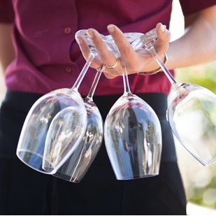 Una cameriera con in mano quattro calici di vino vuoti