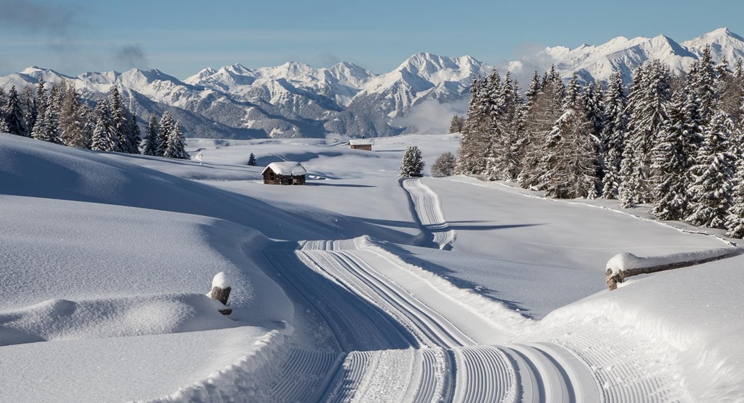 Snowy winter landscape with ski tracks, alpine huts, snow-covered trees and mountain view.