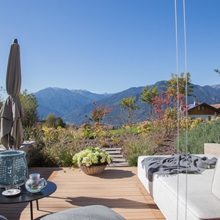 Sonnenterrasse mit Loungemöbeln und Blick auf ein Alpenpanorama unter blauem Himmel.