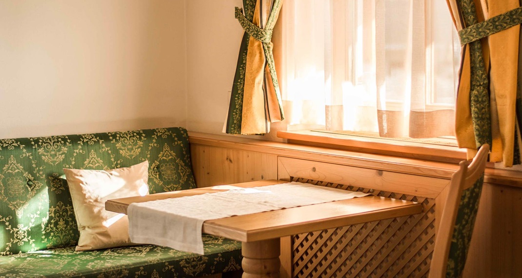 Cozy corner with wooden table, green cushions and sunlight streaming through the window.