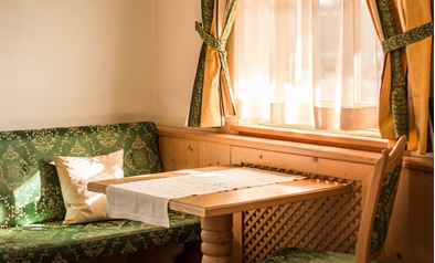 Gemütliche Sitzecke mit Holztisch, grünem Polster und Sonnenschein am Fenster.