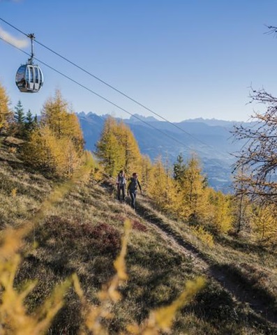 Hikers in autumn forest below cable car with wide mountain panorama in the background.