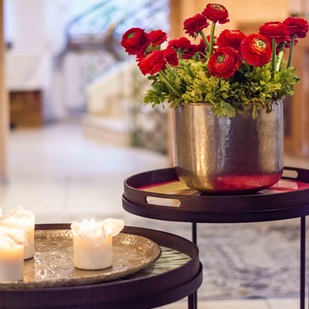 Interno decorativo con ranuncoli rossi in un vaso di metallo e diverse candele accese su tavolini eleganti