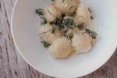 Gnocchi fatti in casa con schiuma, parmigiano e erbe fresche su un piatto bianco.