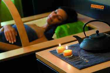 Woman relaxing in spa with lit candles and tea in foreground