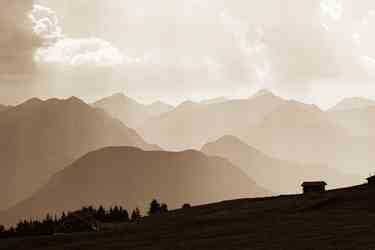 Hütten auf Almwiese vor mehreren Bergketten im Dunst und sepiafarbenes Licht.