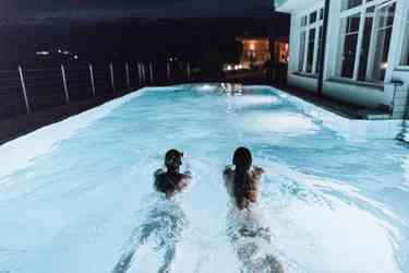 Zwei Personen schwimmen nachts im Außenpool