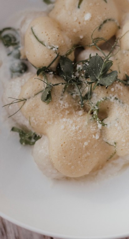 Homemade gnocchi with foam, parmesan and fresh herbs on a white plate.